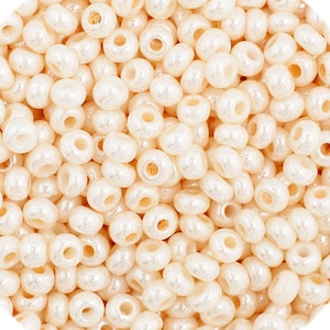 May include: A close-up image of a pile of small, round, white beads with a pearlescent finish. The beads are uniform in size and shape, and they have a smooth, glossy surface.
