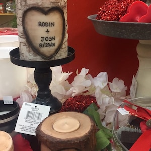 May include: Two birch bark candles with a heart design. The larger candle has the text "Robin + Josh 8/25/01" on the front. The smaller candle is on a wooden base.