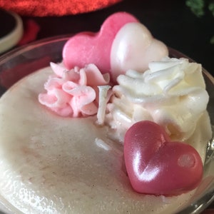 May include: A clear glass jar filled with a white creamy substance topped with pink and white whipped cream and pink heart-shaped candies.