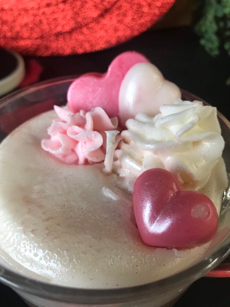 May include: A clear glass jar filled with a white creamy substance topped with pink and white whipped cream and pink heart-shaped candies.