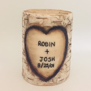 May include: A white cylindrical candle with a birch bark design. A heart is carved into the candle with the names "Robin + Josh" and the date "8/25/01" inscribed inside.