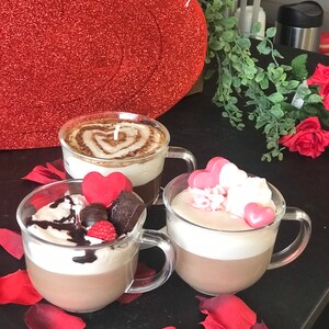 May include: Three mugs of hot chocolate with different toppings. The first mug has a heart design in the chocolate, the second mug has chocolate shavings, a red heart, and a raspberry, and the third mug has pink heart-shaped candies and white whipped cream.