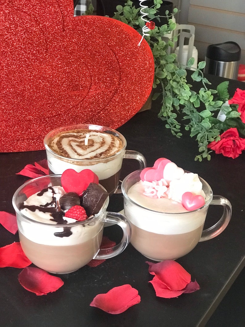 May include: Three mugs of hot chocolate with different toppings. The first mug has a heart design in the chocolate, the second mug has chocolate shavings, a red heart, and a raspberry, and the third mug has pink heart-shaped candies and white whipped cream.