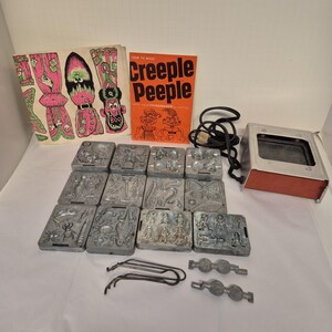 May include: A vintage Creeple Peeple Thingmaker set. The set includes molds with various monster designs, a booklet titled "How to Make Creeple Peeple", and a metal heating unit. The molds are gray, and the booklet is orange and white.