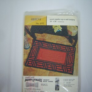 May include: A vintage punch needle rug kit in a plastic package. The kit features a rug design with a red center and a black geometric border. The package reads "ORIENT No. 695" and "24 x 36 finished size". The kit includes Aunt Lydia's heavy rug yarn.