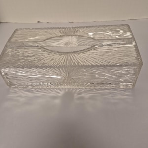 May include: A rectangular clear glass tissue box cover featuring a pressed sunburst or starburst pattern radiating from the center of each side and the top surface, with a central oval opening for dispensing tissues.