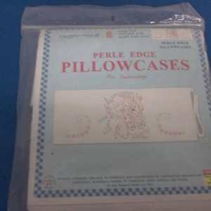 May include: A package of Perle Edge Pillowcases for embroidery. The package has a light blue border with a checkered pattern. The pillowcase design features a floral and horse design in pink and white.