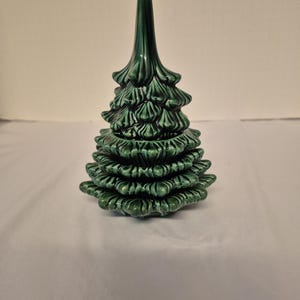May include: A ceramic Christmas tree figurine in a glossy, dark green glaze. The tree has a layered design with detailed, textured branches and a pointed top. The figurine is a decorative item.