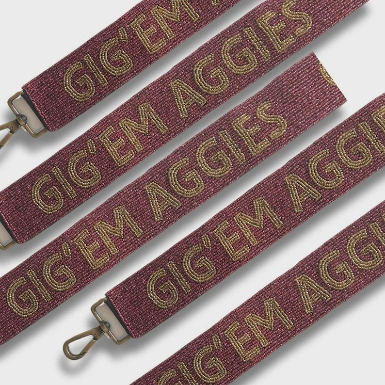 May include: Maroon beaded straps with the text "GIG' EM AGGIES" in gold. The straps have metal clasps on each end. The image shows multiple straps at different angles, creating a repeating pattern. The straps are likely for a bag or purse.