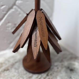 May include: A dark brown wooden display stand with multiple wooden tags. The tags are arranged around a central post and are engraved with the name "Neumann". The stand has a conical base and a smooth, polished finish.