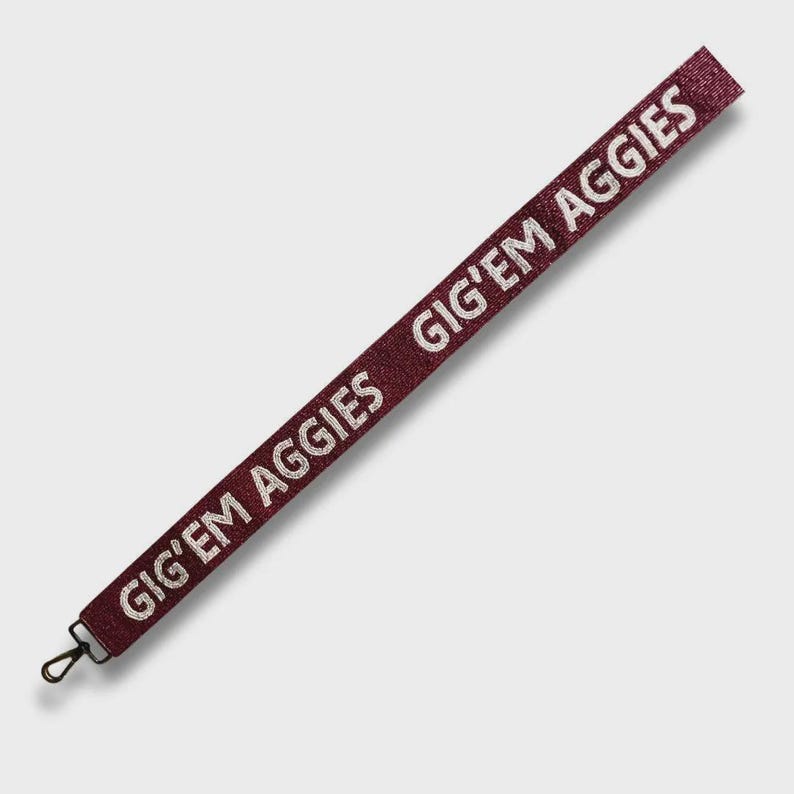 May include: Maroon lanyard with the text "GIG'EM AGGIES" in white. The lanyard has a black metal clasp at the end. The lanyard is angled diagonally across the frame.