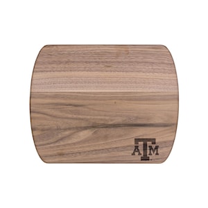 Puede incluir: Una tabla de cortar de madera marrón con un borde redondeado y un logotipo de Texas A&M grabado en la esquina inferior derecha.