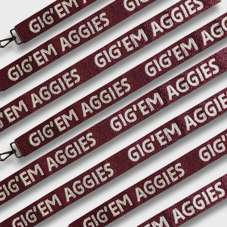 May include: Maroon lanyards with the text "GIG'EM AGGIES" in white. Each lanyard has a black metal clasp. The lanyards are arranged diagonally across the image.