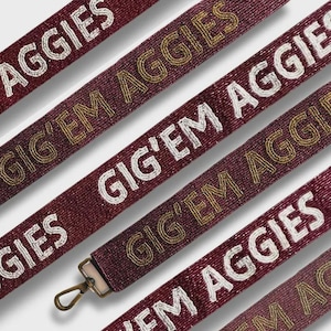May include: Close-up of maroon beaded straps with the words "AGGIES" and "GIG'EM AGGIES" in white and gold beads. One strap has a metal clasp. The straps are angled across the frame.