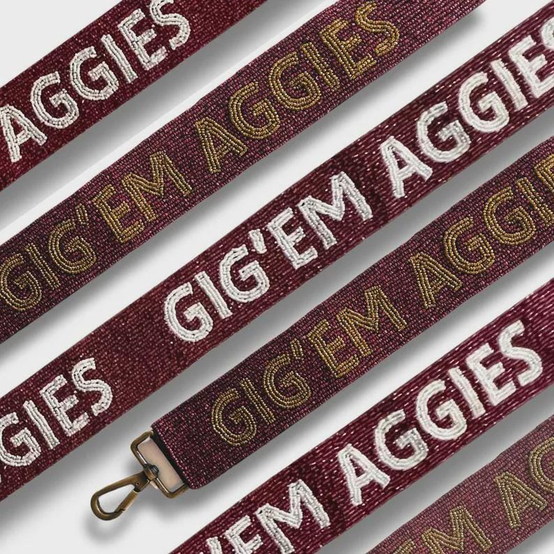 May include: Close-up of maroon beaded straps with the words "AGGIES" and "GIG'EM AGGIES" in white and gold beads. One strap has a metal clasp. The straps are angled across the frame.