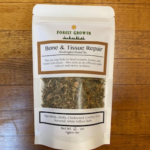 May include: A white pouch with a brown label that reads "Forest Growth Bone & Tissue Repair Handcrafted Herbal Tea". The label also lists the ingredients: Alfalfa, Chickweed, Comfrey Root, Horsetail, White Willow Bark. The pouch contains a blend of dried herbs and has a net weight of 2 ounces. The tea is caffeine-free.
