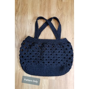 Op de afbeelding: Een marineblauwe gehaakte tote bag met een uniek openwerk ontwerp. De tas heeft twee stevige handvatten en een ronde vorm. De tekst "Pattern Only" is zichtbaar op een klein label.