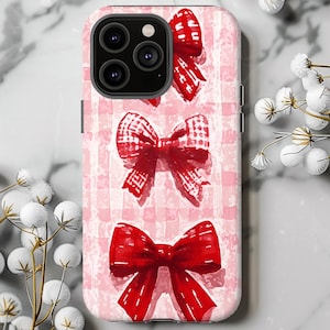 May include: A pink and white checkered phone case with three red bows. The bows are in a vertical line and have a gingham pattern.