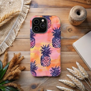 May include: A pink, orange and yellow phone case with a pattern of purple pineapples. The case has a cutout for the camera lens.