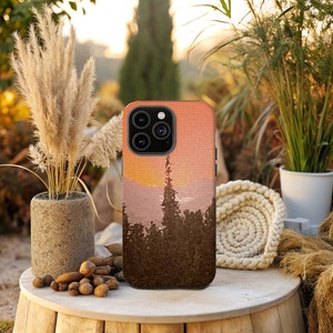 May include: A phone case featuring a pixelated sunset and forest scene. The case is brown and orange with a black camera lens.