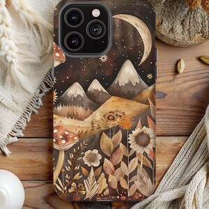 May include: A phone case with a whimsical illustration of a moon, mountains, mushrooms, and flowers in a watercolor style. The background is a dark brown with stars and a crescent moon.