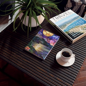 Peut inclure: Un carnet de notes coloré de style vitrail avec une scène de coucher de soleil et des étoiles. Le carnet est posé sur une table en bois foncé avec une tasse de café et un magazine de voyage.