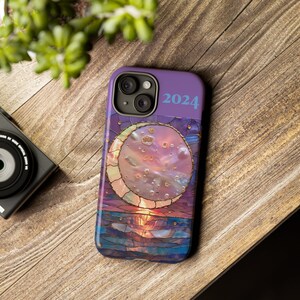 Peut inclure: Coque de téléphone violette avec un motif de vitrail représentant un croissant de lune sur un coucher de soleil. L'année 2024 est imprimée en haut de la coque.