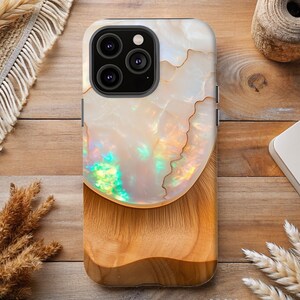 May include: A phone case with a white iridescent design and a wood grain pattern on the bottom. The case has a raised camera bump with three lenses.