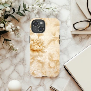 May include: A white iPhone case with a floral design featuring a large, light brown flower and intricate, delicate leaves. The case has a black camera bump with two lenses.