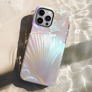 May include: A pearlescent phone case with a seashell design. The case has a white and iridescent finish, with a textured, fan-shaped pattern. The phone case is lying in water, creating a reflective effect.