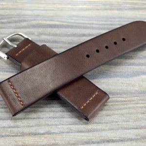 Può includere: Un cinturino da orologio in pelle marrone con una fibbia argentata. Il cinturino è cucito sui bordi e ha cinque fori per regolare la dimensione.