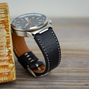 May include: A black leather watch strap with white stitching. The strap is attached to a silver watch with a black face.