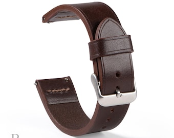 May include: A dark brown leather watch strap featuring a smooth finish, a silver-toned metal buckle, a matching leather keeper loop, and integrated spring bar pins at the attachment points. The strap is curved in a semi-circular shape.