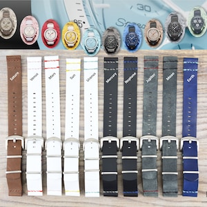 May include: A selection of leather watch straps in different colours, each labelled with a planet name. The straps have silver buckles. Above, there are several watches with different coloured faces. The background is a light wood surface.