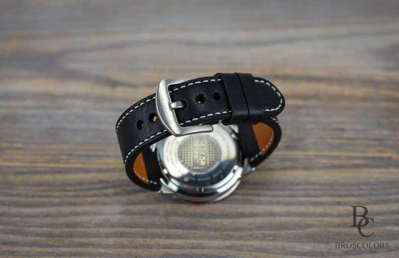 May include: A black leather watch strap with white stitching and a silver buckle. The strap is attached to a silver watch with a black face.