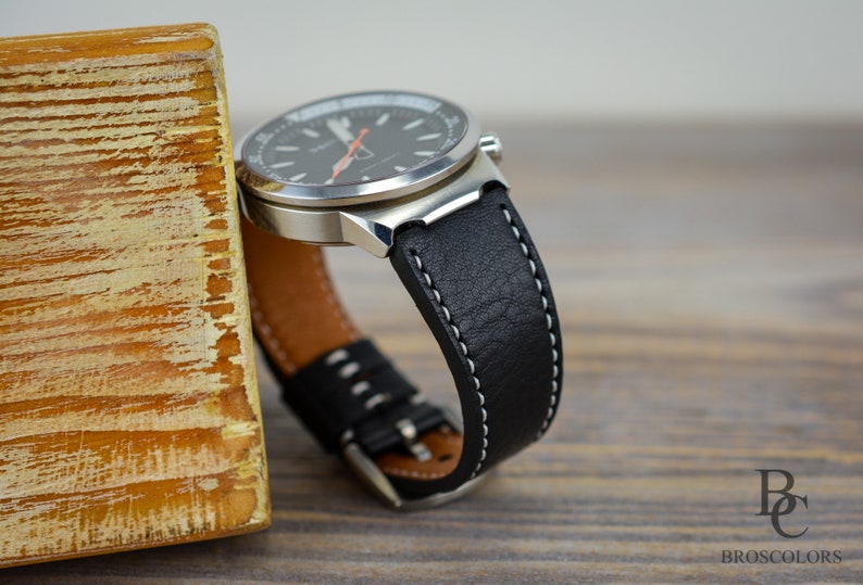 May include: A black leather watch strap with white stitching. The strap is attached to a silver watch with a black face.