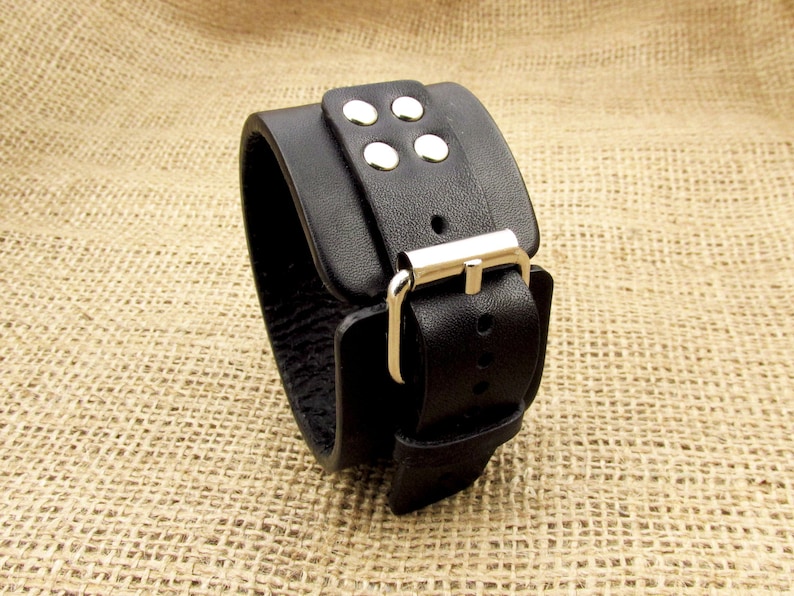 May include: Black leather cuff bracelet with a silver buckle and four silver studs.