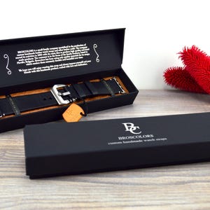 May include: A black leather watch strap with a silver buckle in a black box. The box has the text "Broscolors Custom Handmade Watch Straps" printed on it.