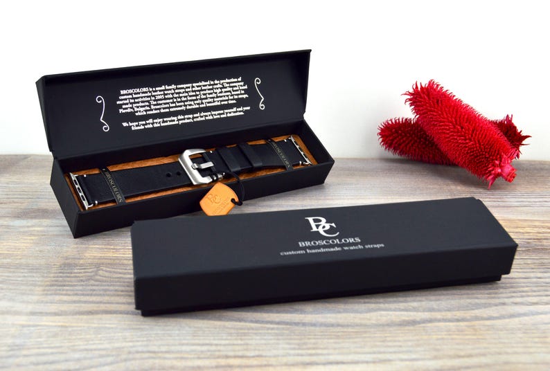 May include: A black leather watch strap with a silver buckle in a black box. The box has the text "Broscolors Custom Handmade Watch Straps" printed on it.