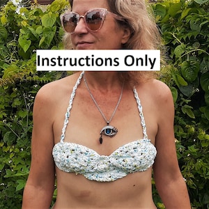 Könnte beinhalten: Eine Frau trägt ein weißes Häkel-Bikini-Oberteil mit einer blauen Augen-Anhängerkette. Das Bikini-Oberteil hat einen gewellten Rand und ist aus einem zarten Häkelstoff gefertigt.