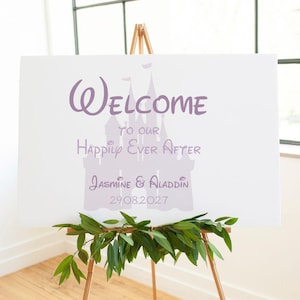 May include: A white sign on a wooden easel, featuring purple text that reads "Welcome to our Happily Ever After". The names "Jasmine & Aladdin" and the date 29.08.2027 are also displayed. Green foliage decorates the bottom of the sign.