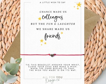 May include: A greeting card with a red string bracelet. The card has text that reads "Chance made us colleagues, but the fun & laughter we share made us friends." The card is on a woven background.