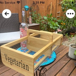 Op de afbeelding: Een houten dienblad met een draadgaas inzet en een handvat. Het dienblad is gelabeld "Vegetarisch" en staat op een blauw-wit betegelde ondergrond.