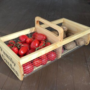 Op de afbeelding: Een houten kist met een draadgaas inzet, met het label "Family Garden", gevuld met rode tomaten en aardappelen.