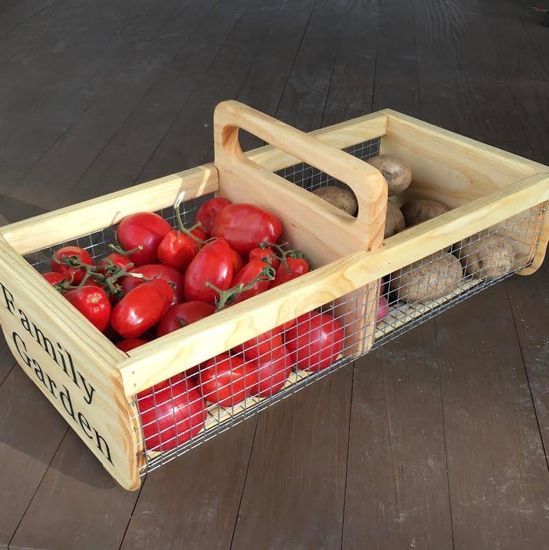 Op de afbeelding: Een houten kist met een draadgaas inzet, met het label "Family Garden", gevuld met rode tomaten en aardappelen.