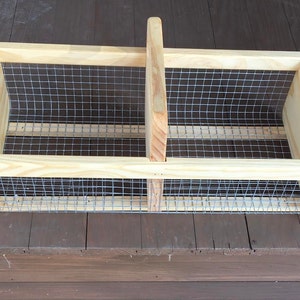 Op de afbeelding: Een houten kist met een gaas van draad en een handvat. De kist is gemaakt van natuurlijk hout en heeft een rustieke uitstraling.