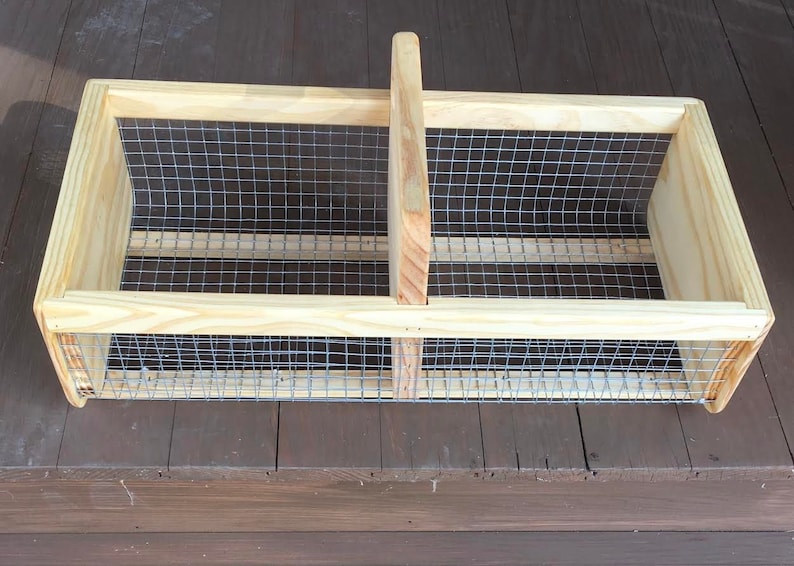 Op de afbeelding: Een houten kist met een gaas van draad en een handvat. De kist is gemaakt van natuurlijk hout en heeft een rustieke uitstraling.