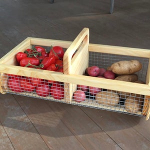 Op de afbeelding: Een houten kist met een draadgaas inzet, verdeeld in twee secties. De linker sectie bevat rode tomaten, en de rechter sectie bevat bruine aardappelen.
