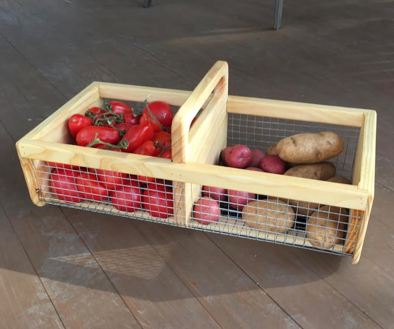 Op de afbeelding: Een houten kist met een draadgaas inzet, verdeeld in twee secties. De linker sectie bevat rode tomaten, en de rechter sectie bevat bruine aardappelen.