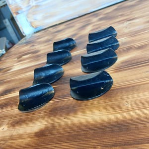 Peut inclure: Huit poignées de tiroir en métal noir avec un design incurvé. Les poignées sont disposées en rangée sur une surface en bois.